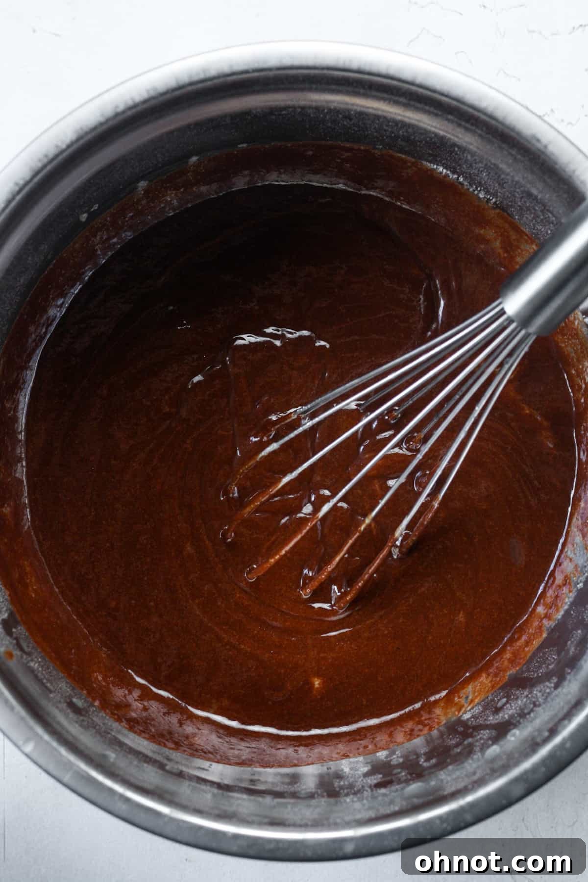 Thick, glossy brownie batter forming in a mixing bowl after combining wet ingredients.