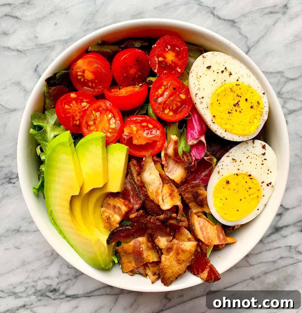 A vibrant and healthy Cobb Salad with mixed greens, crispy bacon, cherry tomatoes, hard-boiled eggs, and sliced avocado, garnished with fresh basil. Perfect for Whole30, Keto, and Paleo diets.