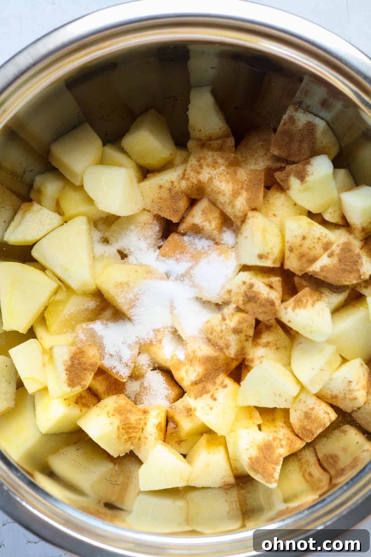 Cubed apples mixed with cinnamon, sugar, and lemon juice in a bowl.