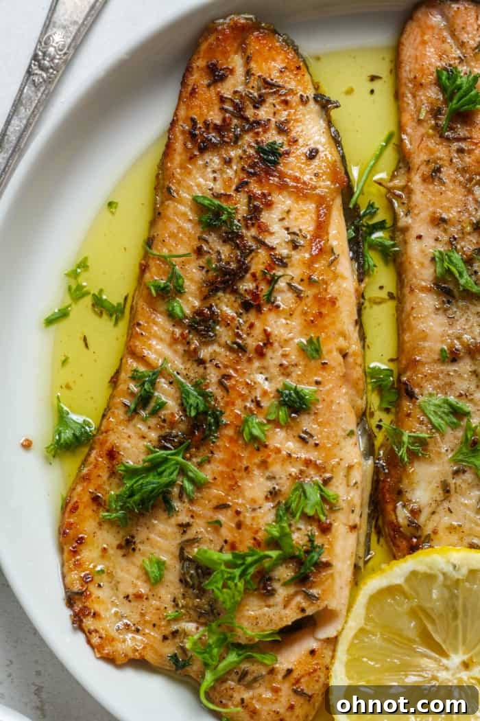 Trout recipe on plate, garnished with fresh herbs and lemon wedges.
