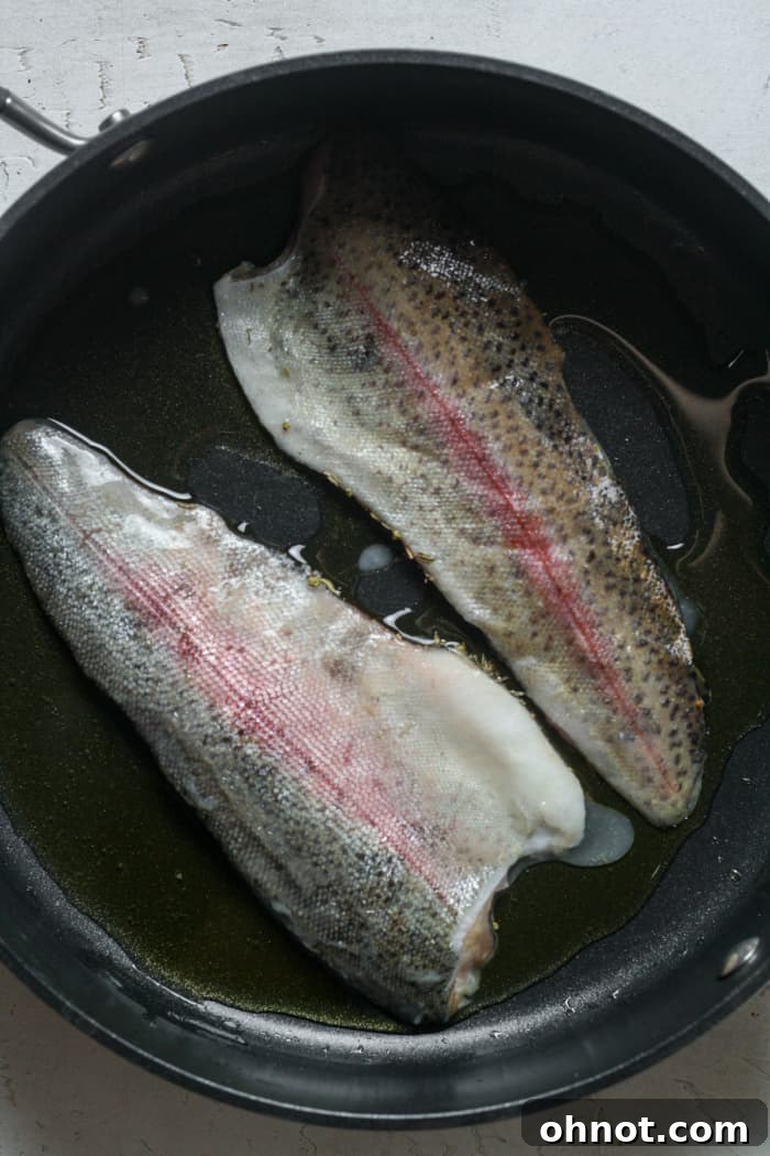 Rainbow trout fillets searing in a hot skillet with olive oil and melted butter.