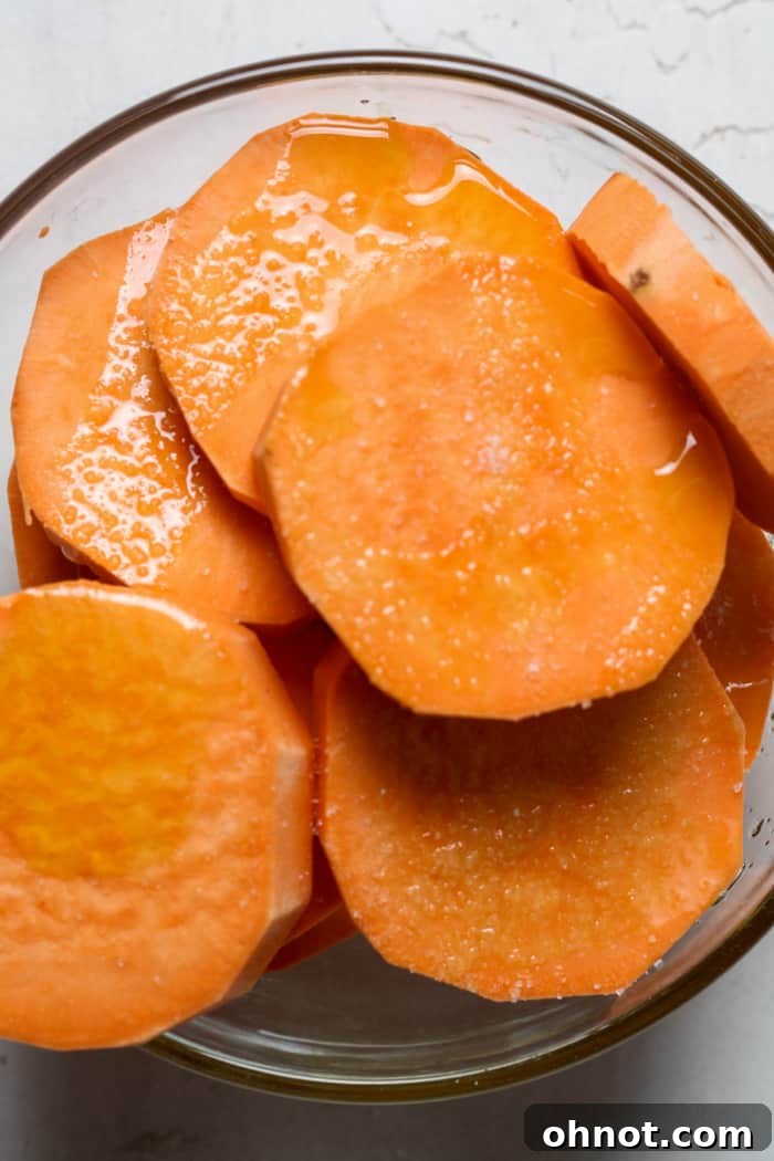 Sweet potato slices tossed with oil and sea salt in a bowl.
