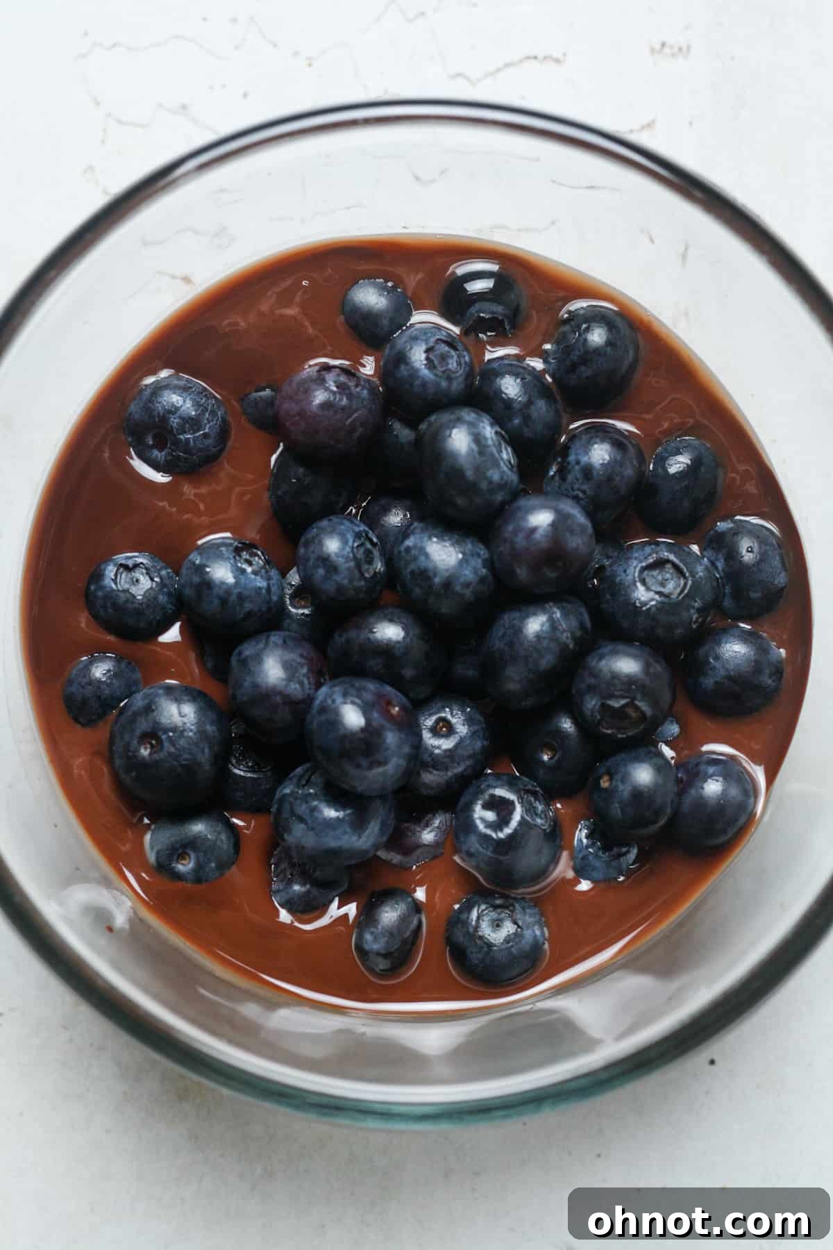 Fresh blueberries gently mixed into the melted chocolate in a bowl, ensuring even coating.