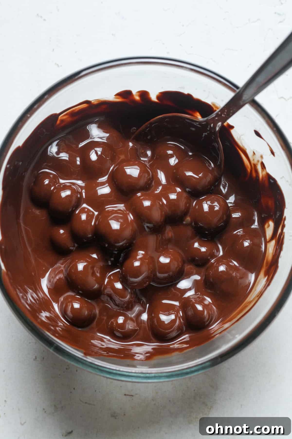 Close-up of blueberries fully coated in rich chocolate mixture, ready for clustering.