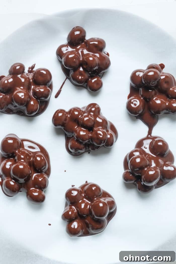 Small clusters of chocolate-covered blueberries placed on parchment paper, awaiting chilling.