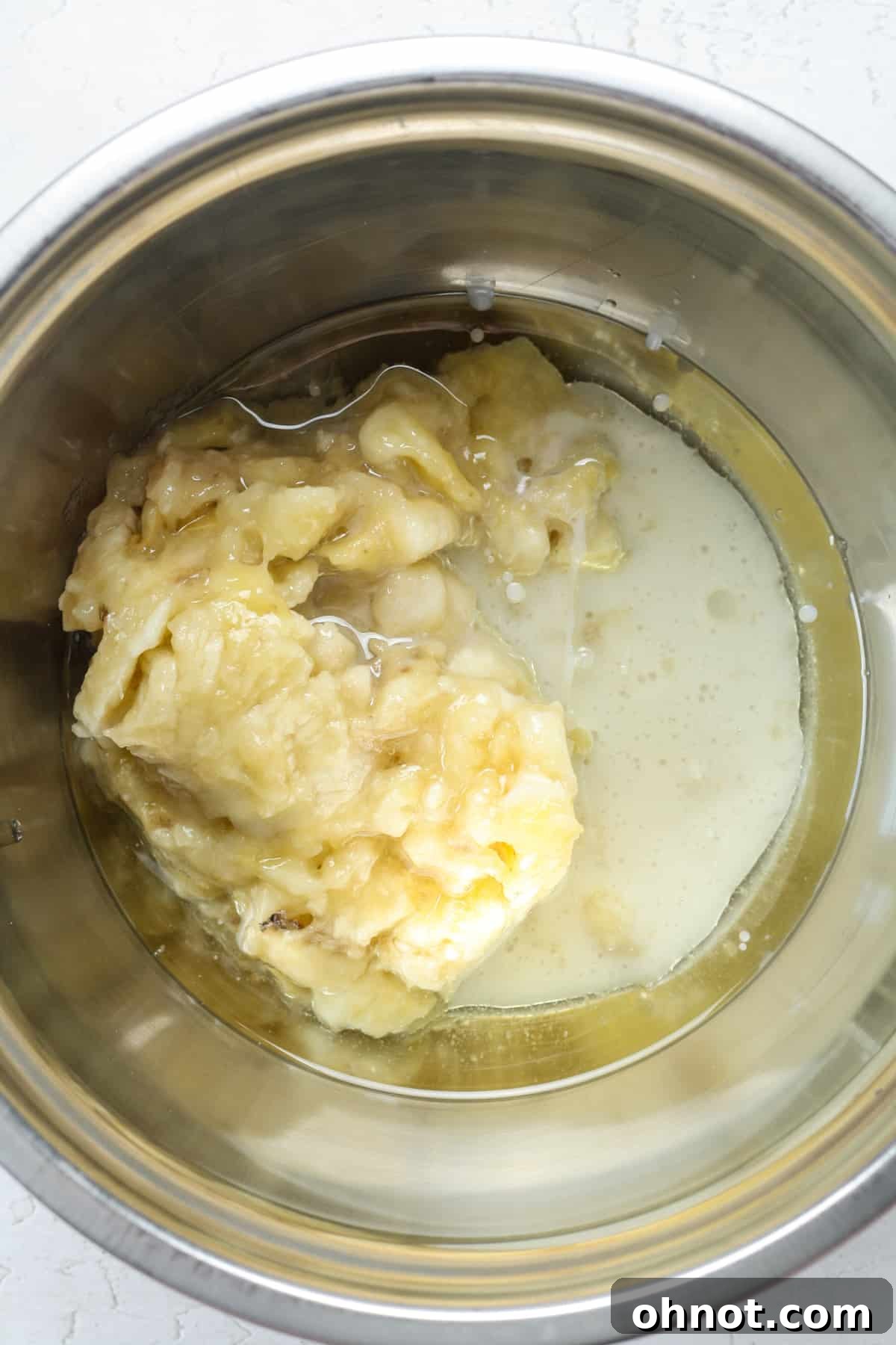 A bowl containing mashed bananas, melted coconut oil, and milk, ready for mixing.