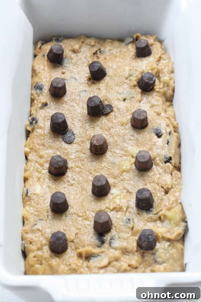 Unbaked banana bread batter in a lined loaf pan, with optional chocolate chips on top.