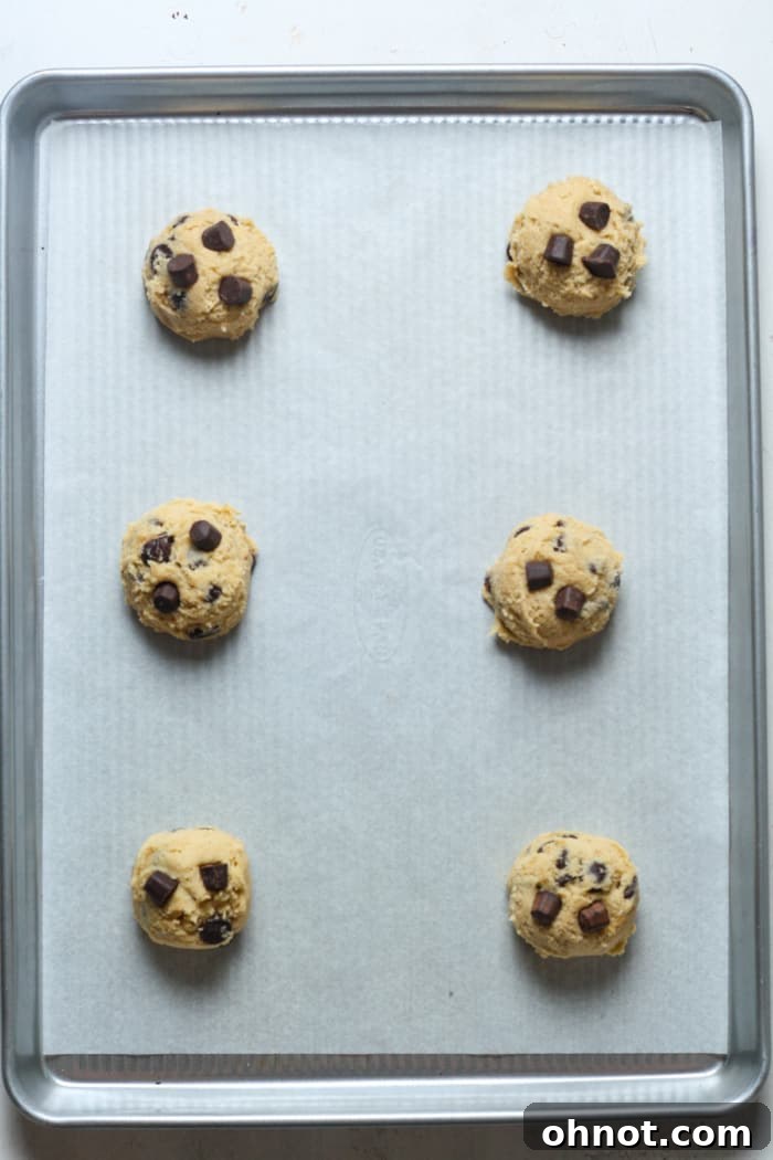 Scoops of gluten-free chocolate chip cookie dough on a parchment-lined baking sheet.