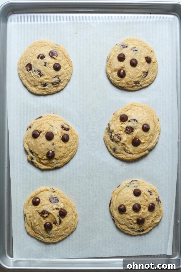 Six freshly baked gluten-free chocolate chip cookies cooling on a baking sheet.