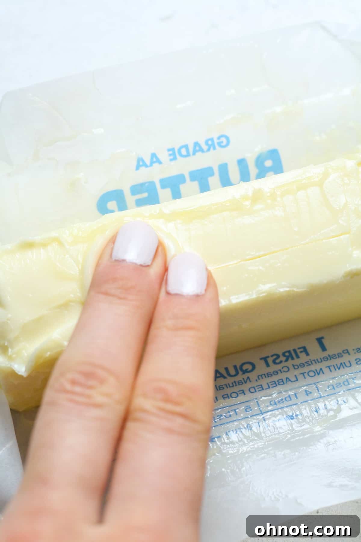 Fingers gently pressing into softened butter to check consistency.