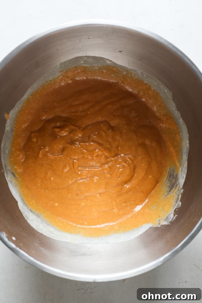 Orange pumpkin pie batter in a bowl, showing the combined wet ingredients before spices are added.