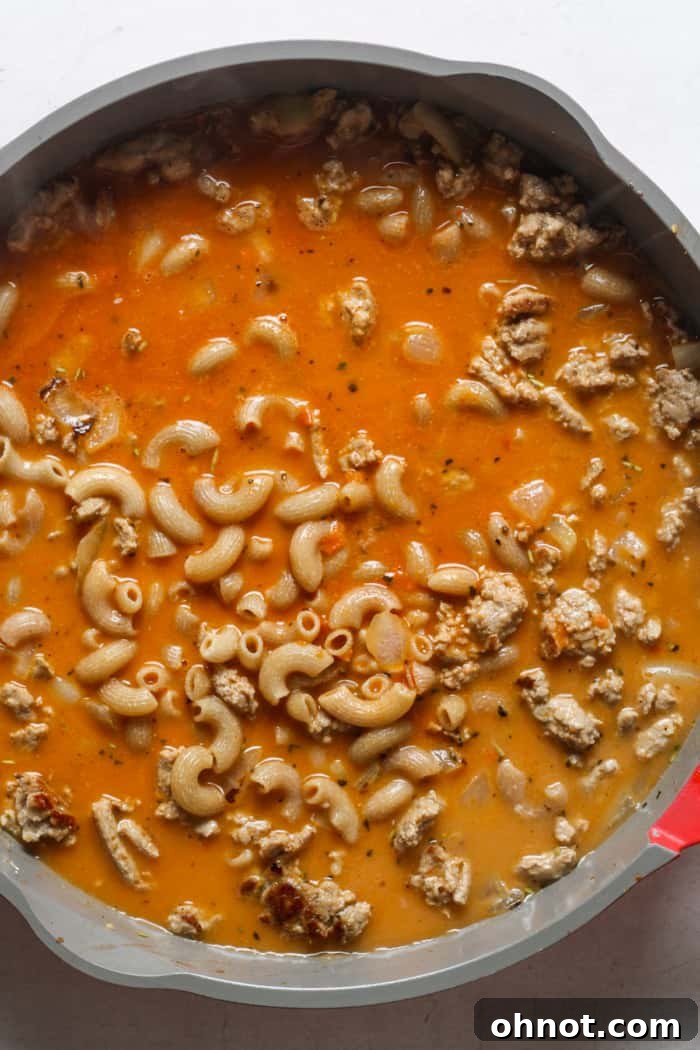 The Healthy Hamburger Helper mixture boiling in a pan, with pasta and sauce simmering together to cook and thicken.