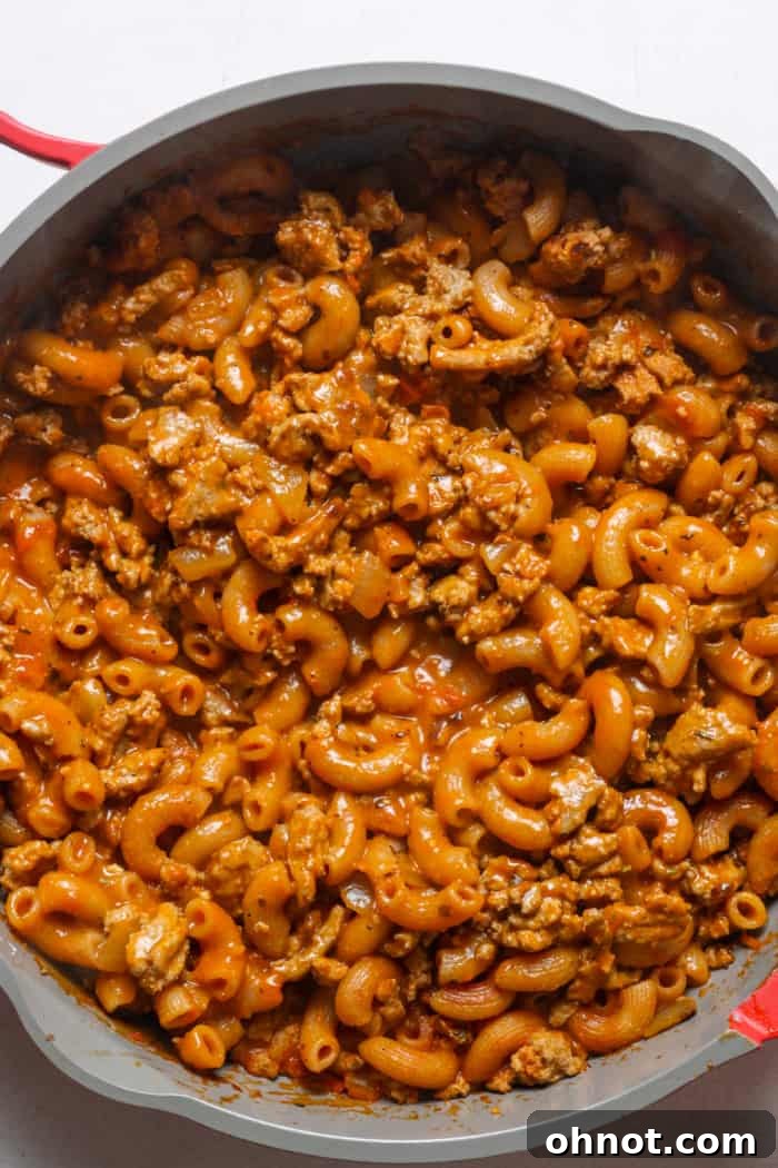 Healthier Hamburger Helper simmering gently in a pan, showing the thickening sauce and cooked pasta for a comforting meal.