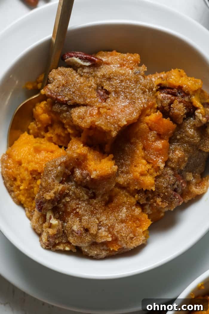 A single serving of gluten-free sweet potato casserole in a white bowl, showing the creamy filling and crunchy topping.