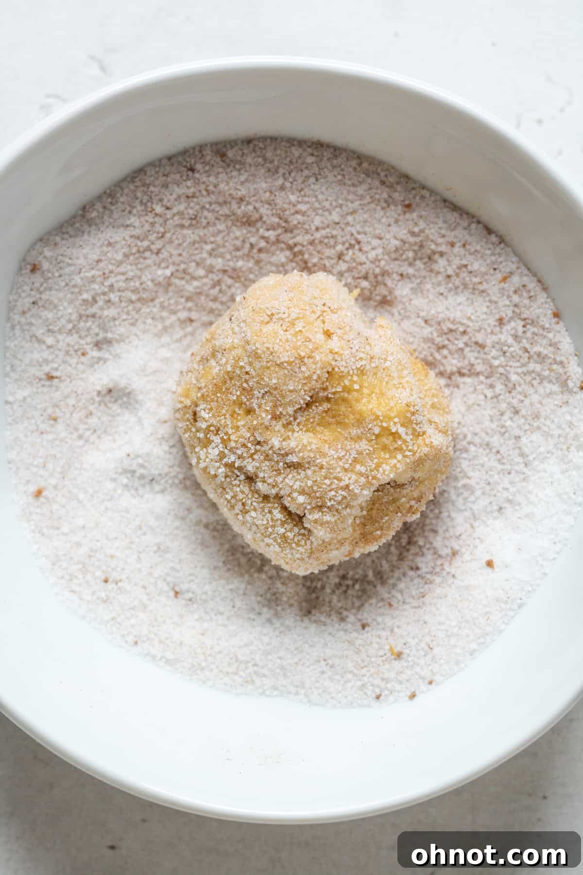 A rolled cookie dough ball being coated in a mixture of cinnamon sugar and pumpkin pie spice.