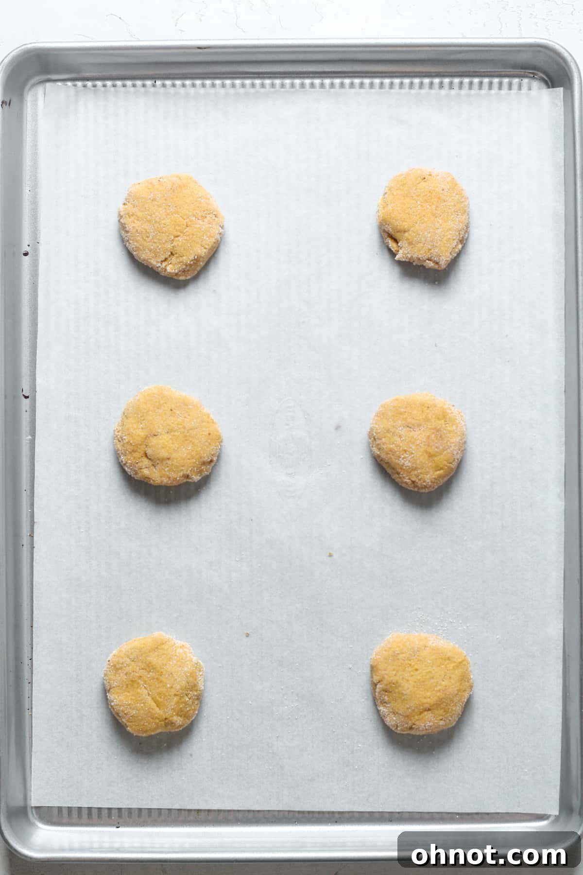 Raw pumpkin snickerdoodle cookies, coated in sugar and flattened, arranged on a parchment-lined baking sheet.