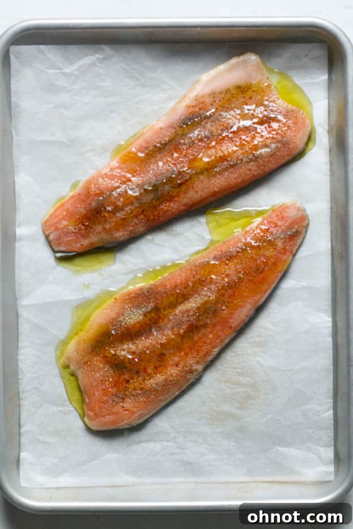 Rainbow trout fillets arranged on a parchment-lined baking pan, drizzled with olive oil and lemon.