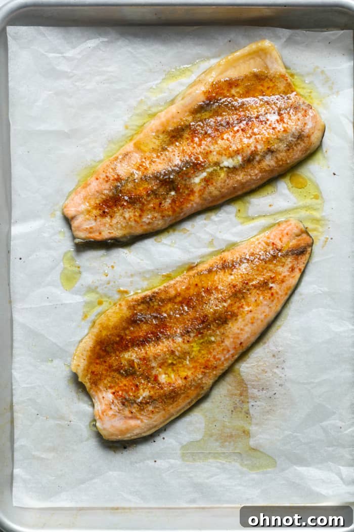 Baked rainbow trout fillets on a pan, showing golden edges and juicy texture.