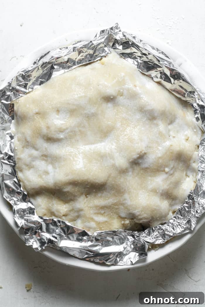 Apple pie with tin foil protecting its edges before baking.
