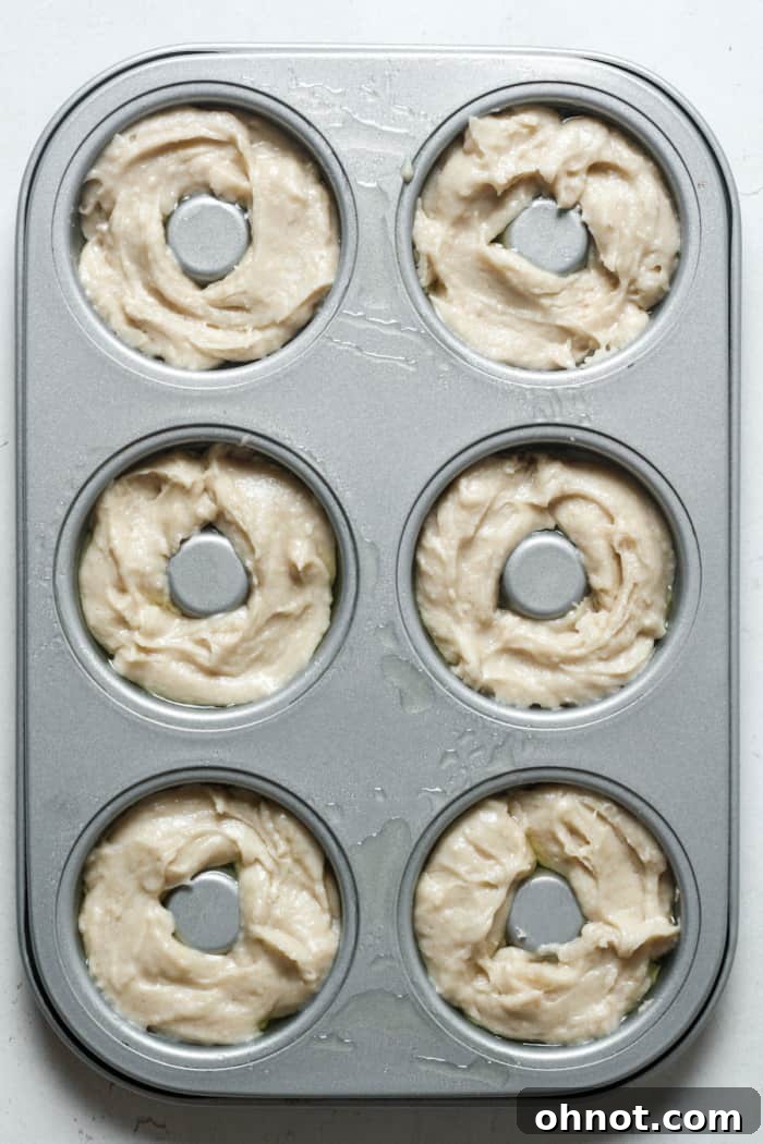 Raw donut batter meticulously placed into a greased donut pan, ready for the oven.