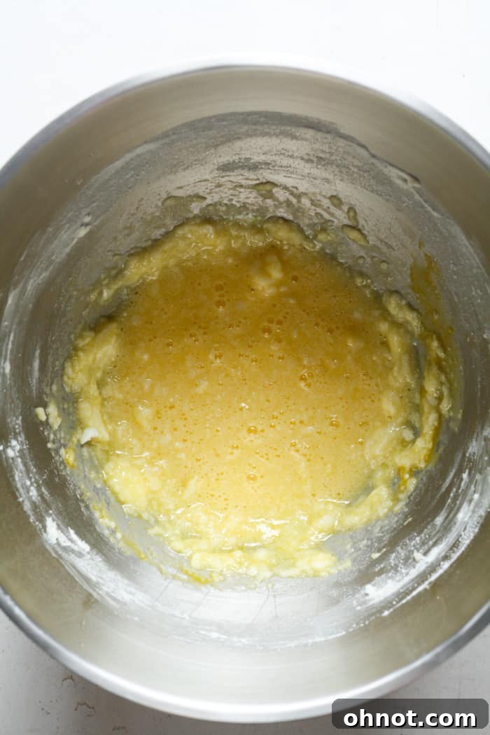 Eggs and vanilla extract being stirred into the creamed butter and sugar mixture in a bowl.