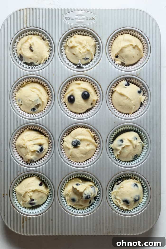 Raw muffin batter scooped into individual muffin liners in a baking pan, ready for the oven.
