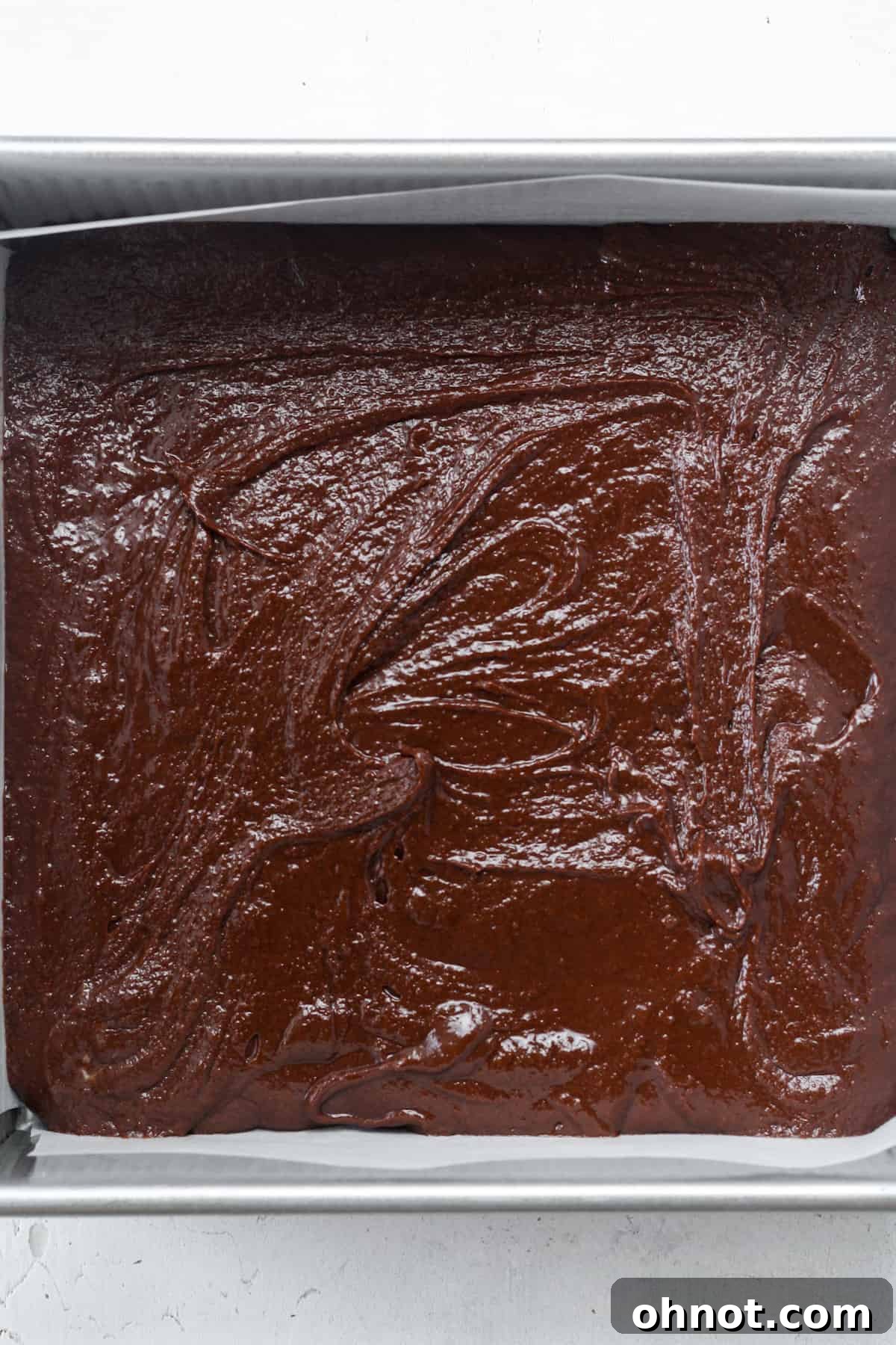 Chocolate brownie batter spread evenly in a square baking pan.