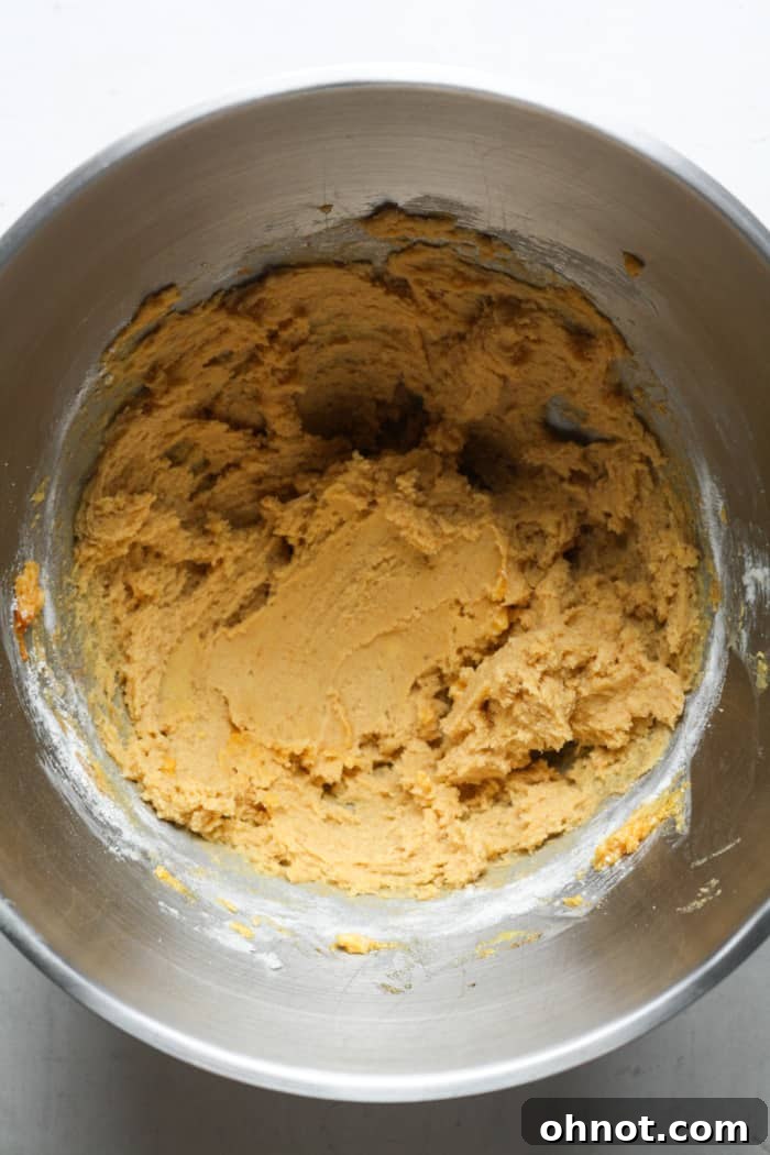 Pumpkin cookie dough in a mixing bowl with dry ingredients added.