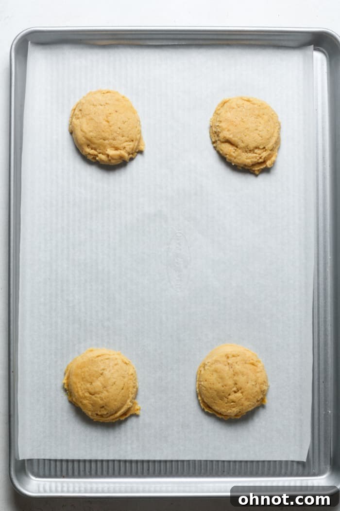 Four scooped and gently flattened orange cookie dough balls on a parchment-lined baking sheet.