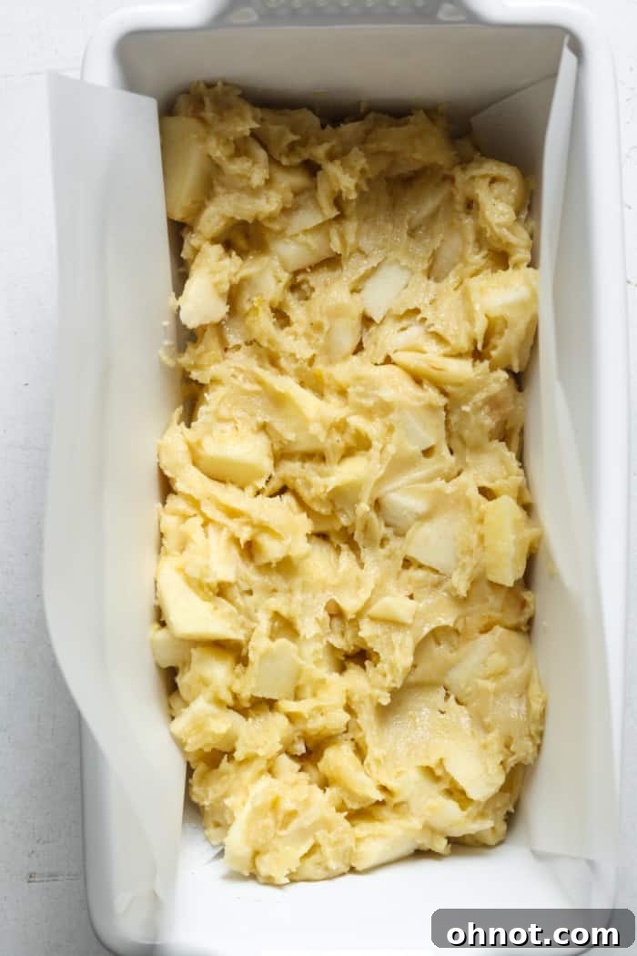 Half of the thick apple bread batter spread in the lined pan.