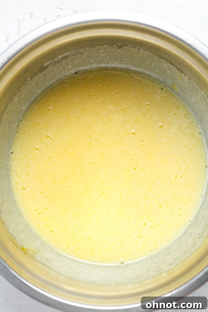 Sugar, melted butter, and eggs being whisked together in a mixing bowl, creating a light and frothy mixture for almond flour brownies.