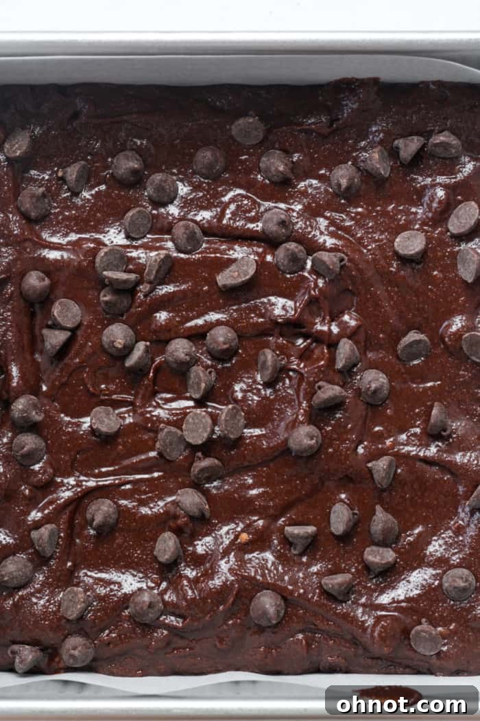 Unbaked almond flour brownie batter poured into a parchment-lined square pan, topped with extra chocolate chips, ready for the oven.
