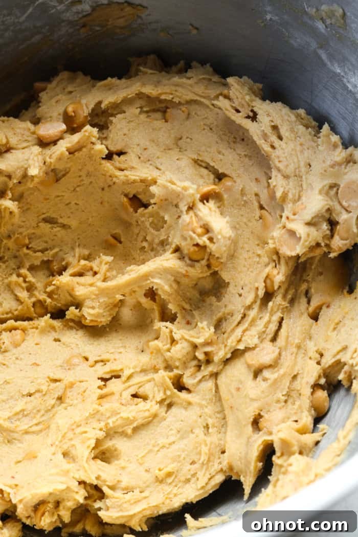Peanut butter chips being folded into the thick cookie dough.