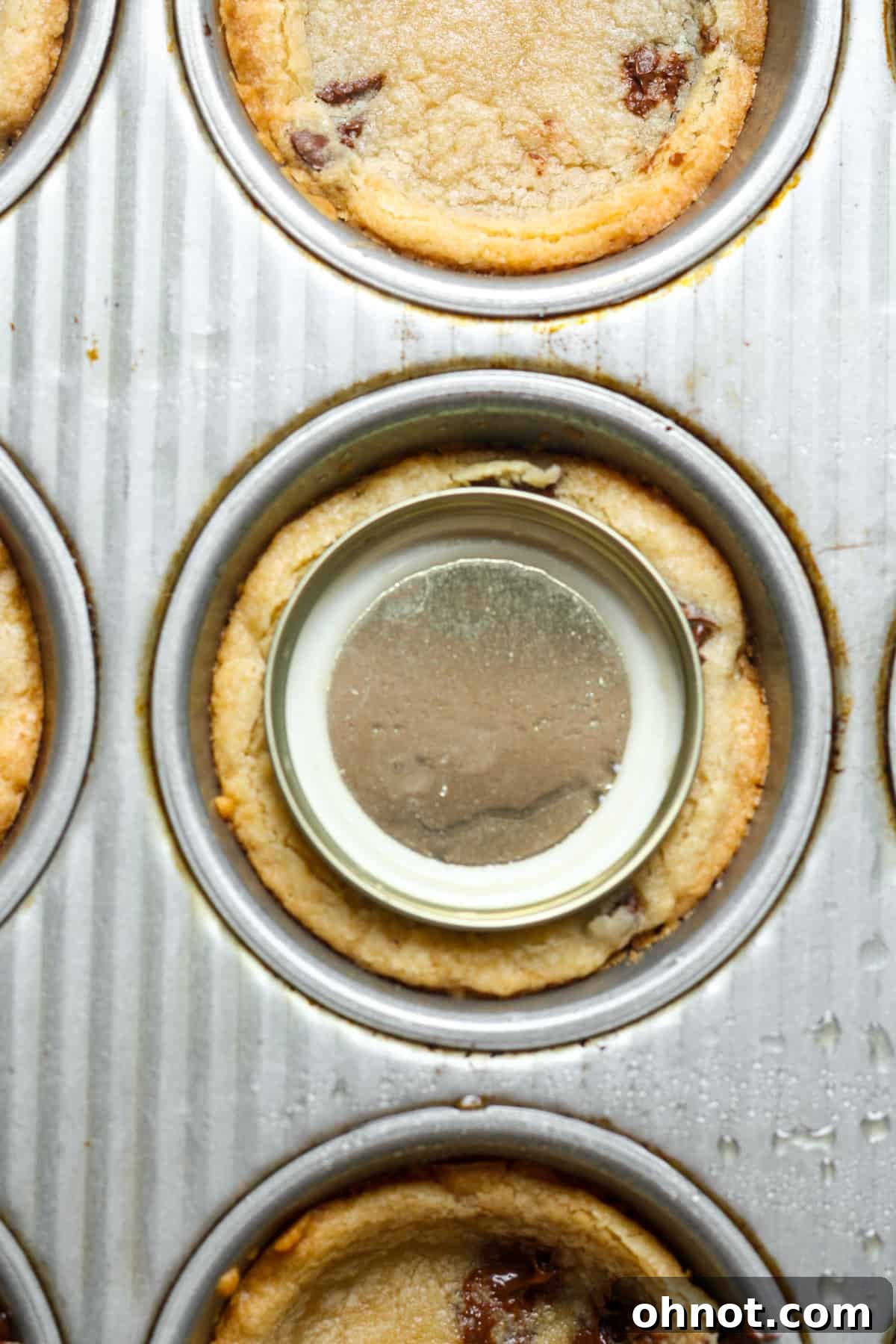 Jar lid pressing into a warm cookie cup to create an indentation.