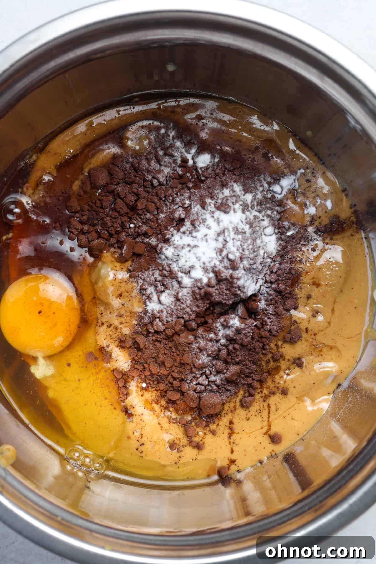 Cracked egg and cocoa powder mixed into a thick, creamy batter in a bowl.