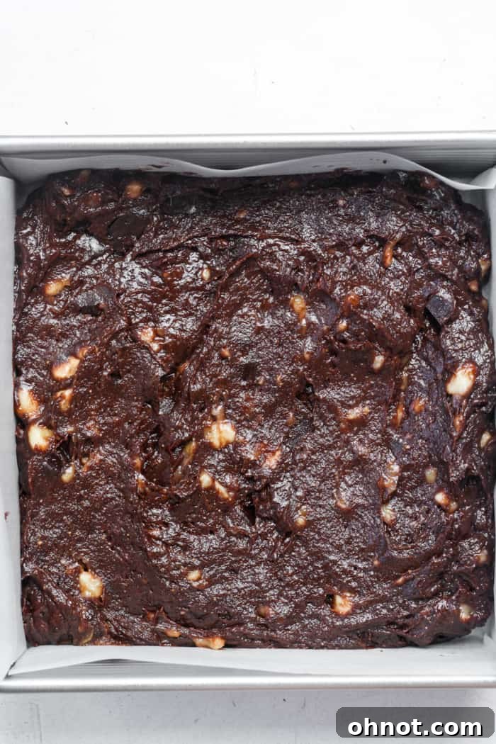 Raw banana brownie batter spread smoothly in a parchment-lined baking pan, ready for the oven.