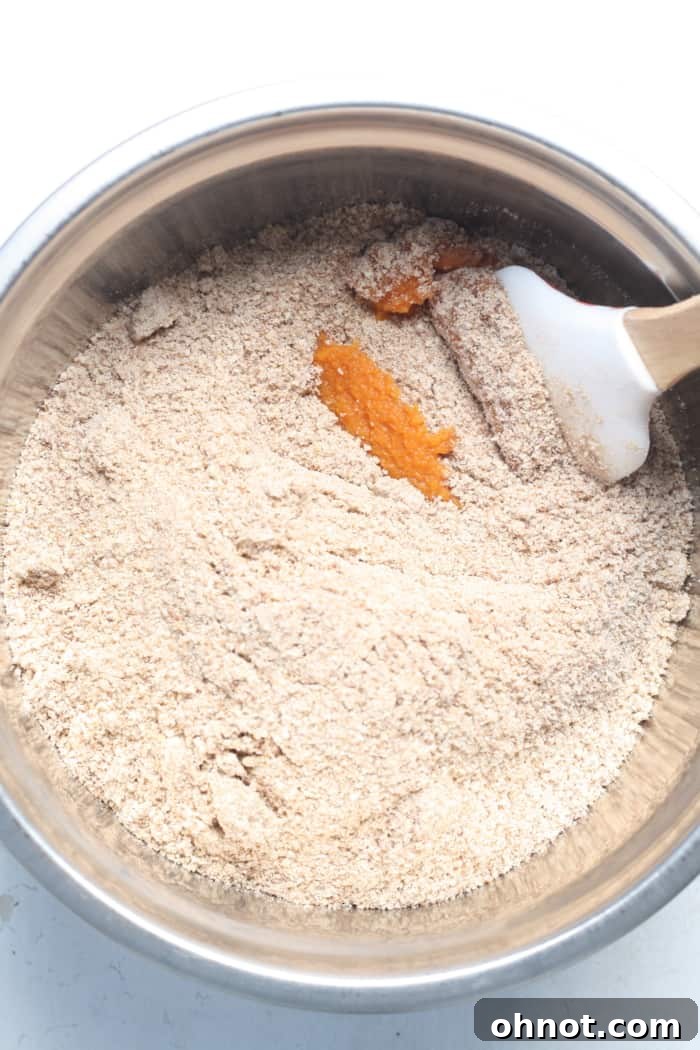 Dry muffin mix being added to a bowl with pumpkin purée.