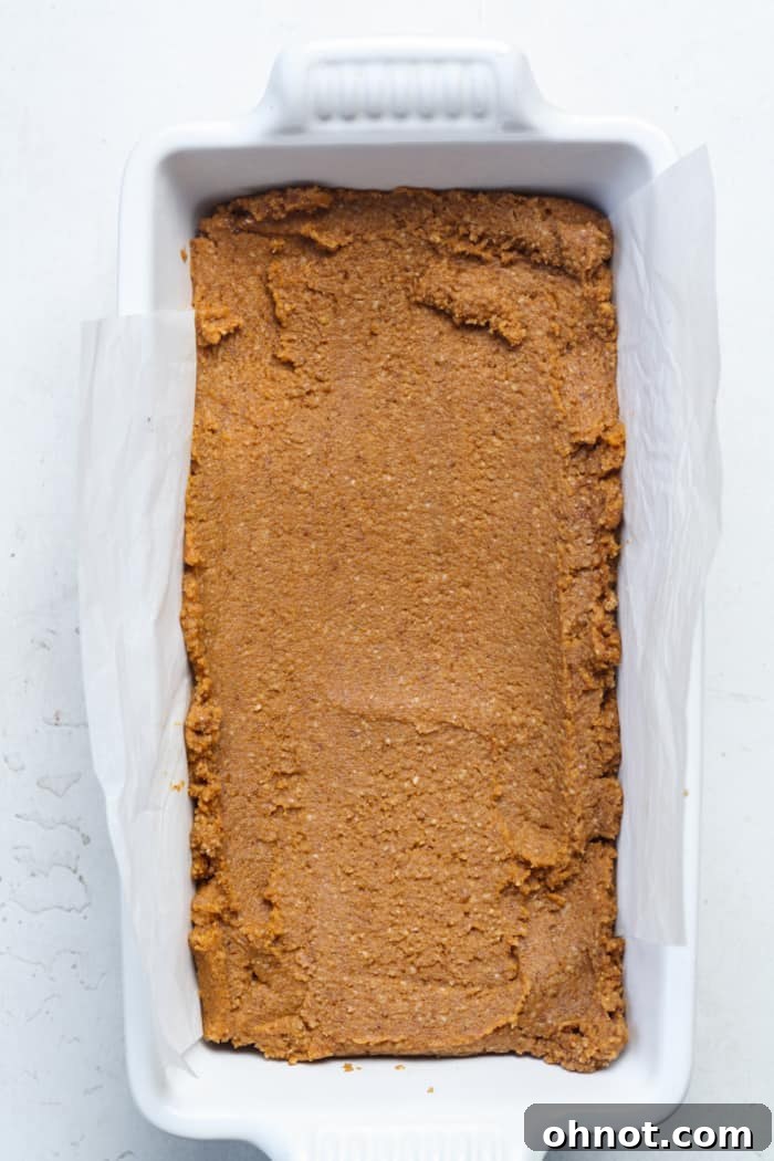 Raw pumpkin bread batter spread evenly in a parchment-lined loaf pan.