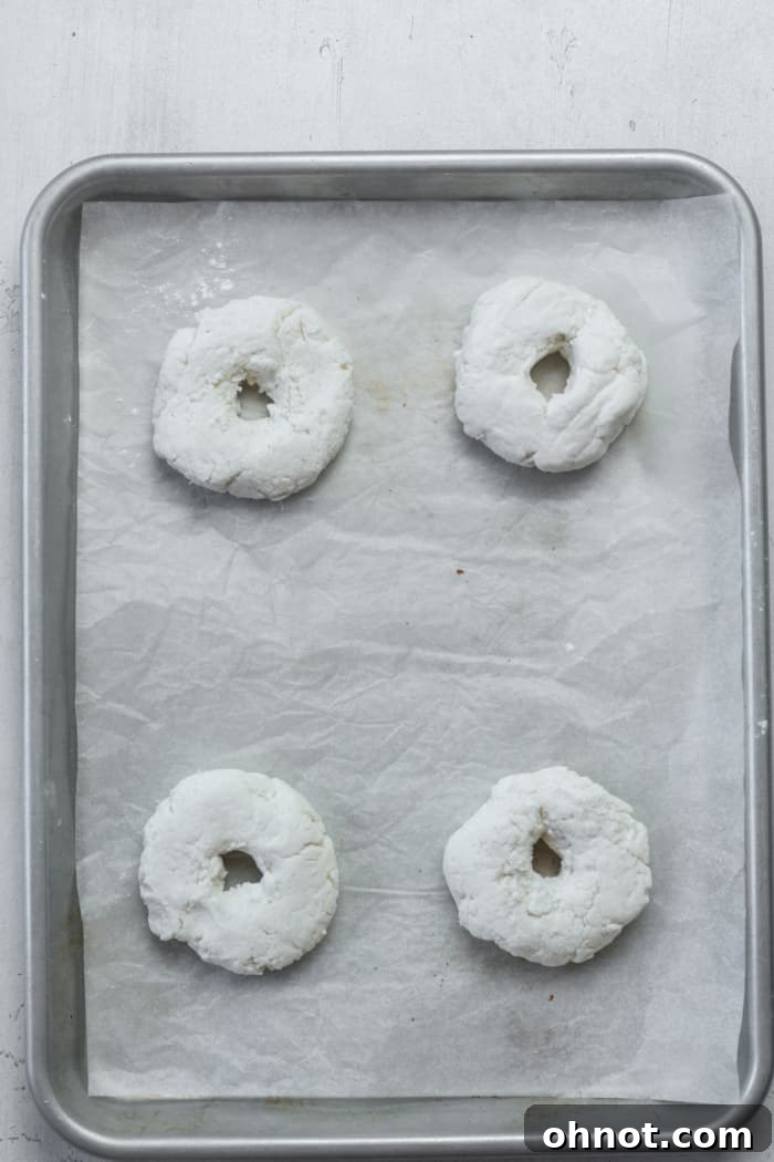 A baking pan with several raw gluten-free bagels arranged on parchment paper.