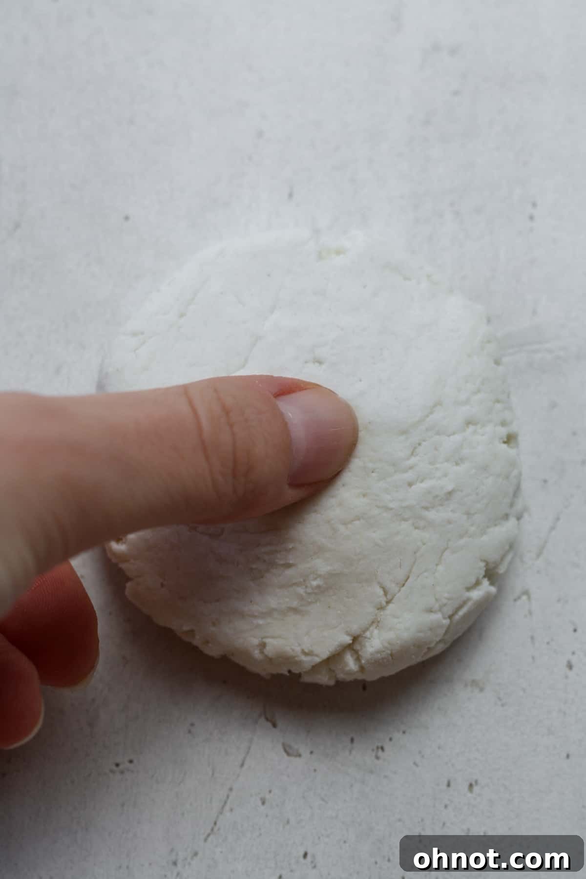 A finger poking a hole in the center of a dough disc.