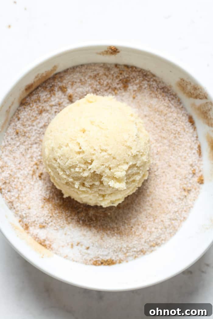 A ball of cookie dough being rolled in the spiced sugar coating.