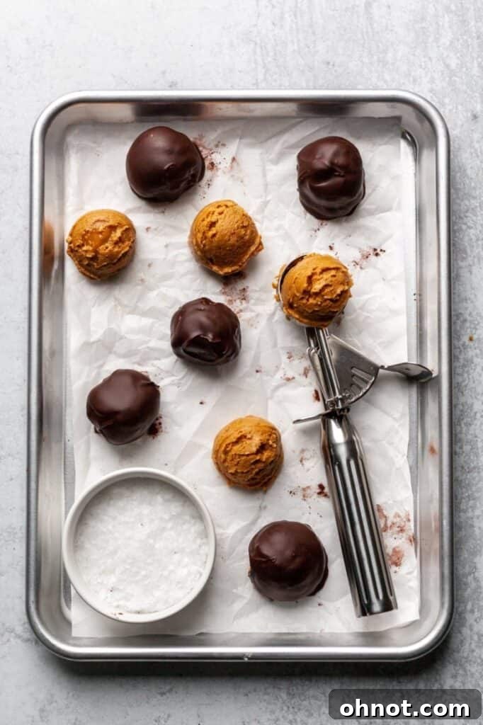 Finished Vegan Paleo Chocolate Covered Almond Butter Balls, perfectly coated and garnished with sea salt, stacked on a white plate.