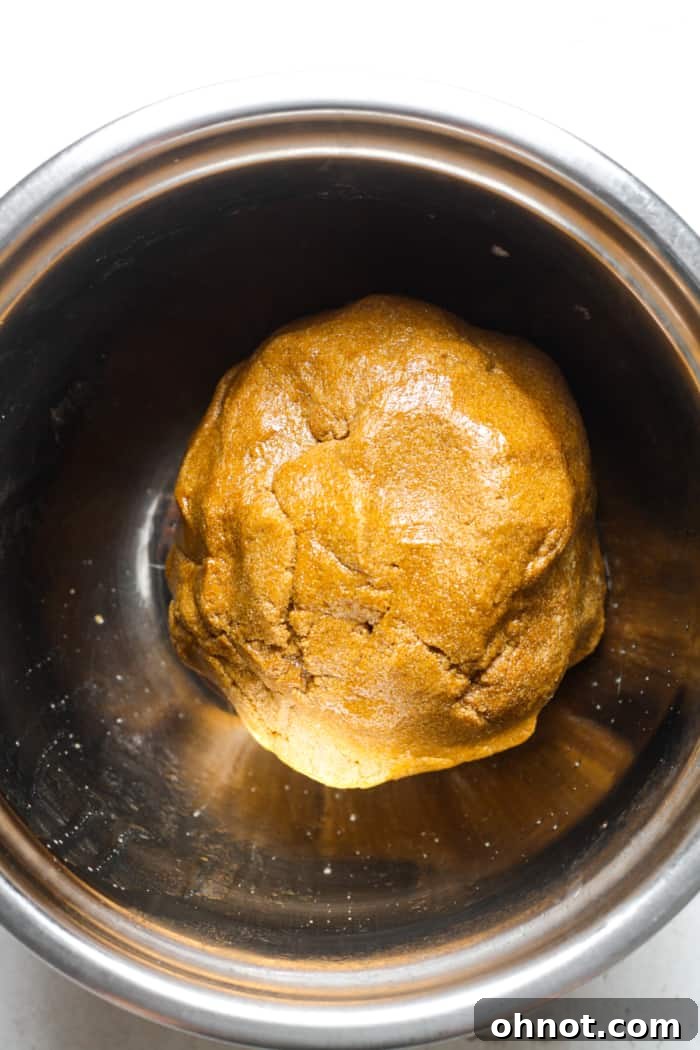 Ball of vegan gingerbread dough covered with plastic wrap in a bowl.