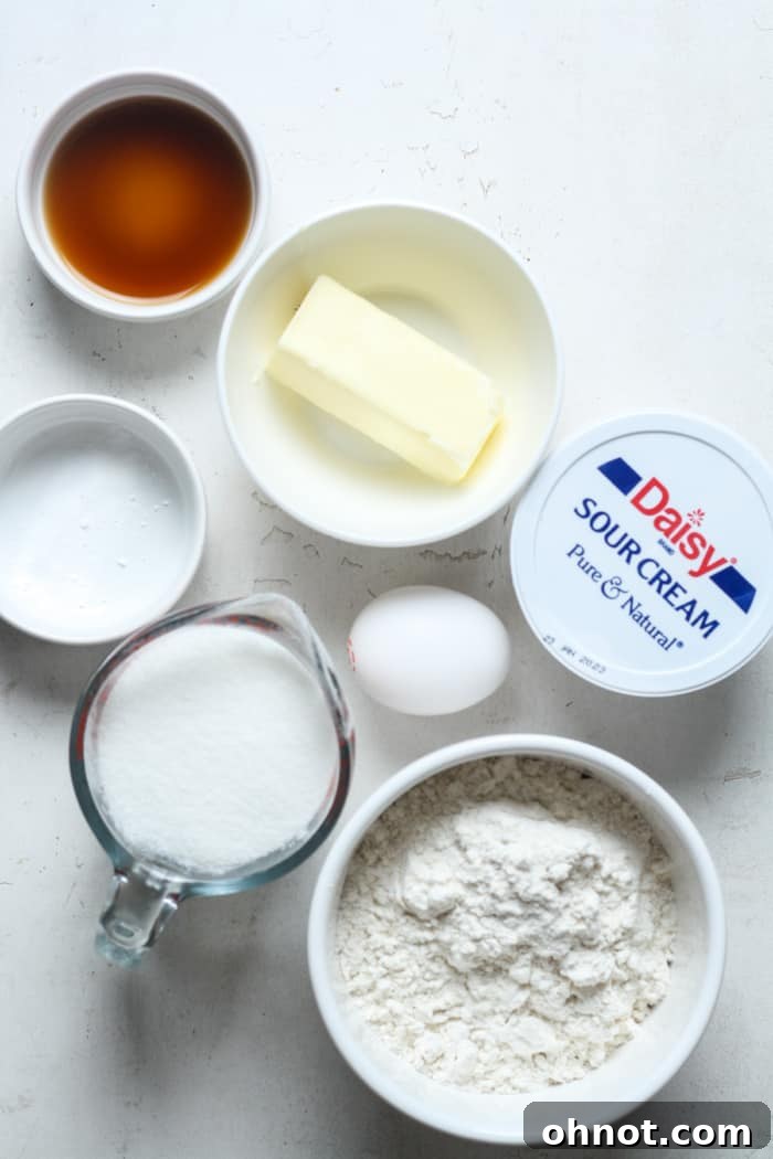 Various ingredients for sour cream cookies laid out on a table, including flour, sugar, butter, and a bowl of sour cream.