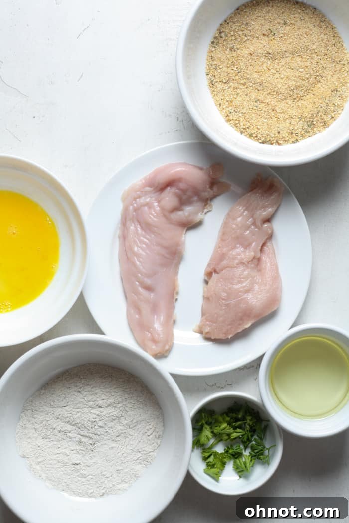 Raw chicken breast prepared for schnitzel, alongside panko breadcrumbs in a bowl.