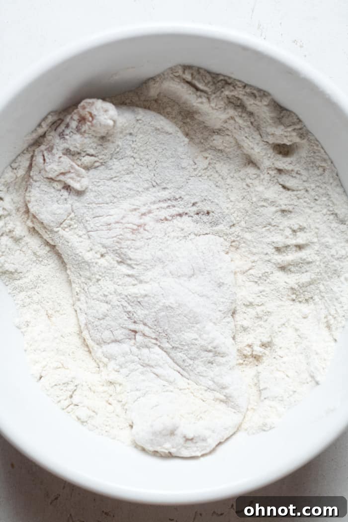 Chicken breast being dredged in flour, ready for the next step in making schnitzel.