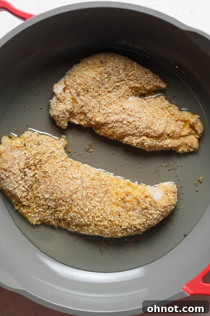 Breaded chicken schnitzel sizzling in a skillet with hot oil, cooking to a golden crisp.