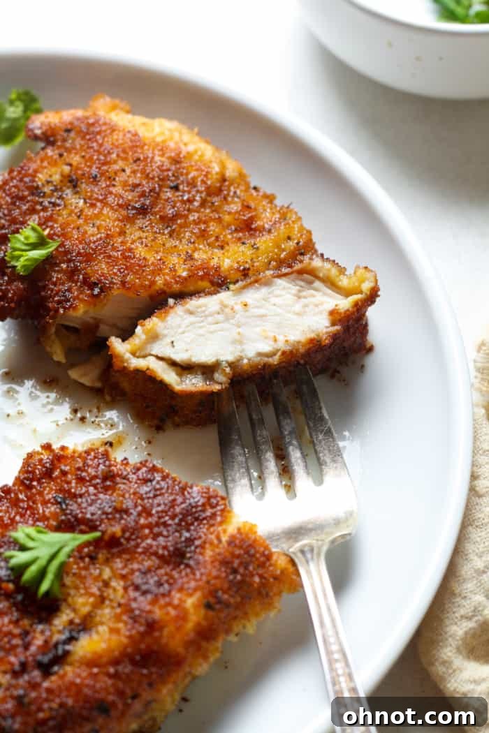A fork holding a piece of white meat chicken schnitzel, showing its juicy interior.