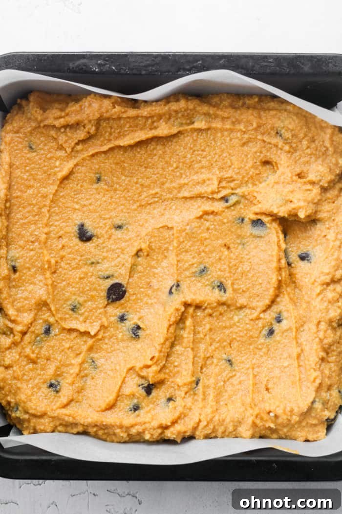 Thick orange pumpkin bar batter smoothly spread into a parchment-lined baking pan.