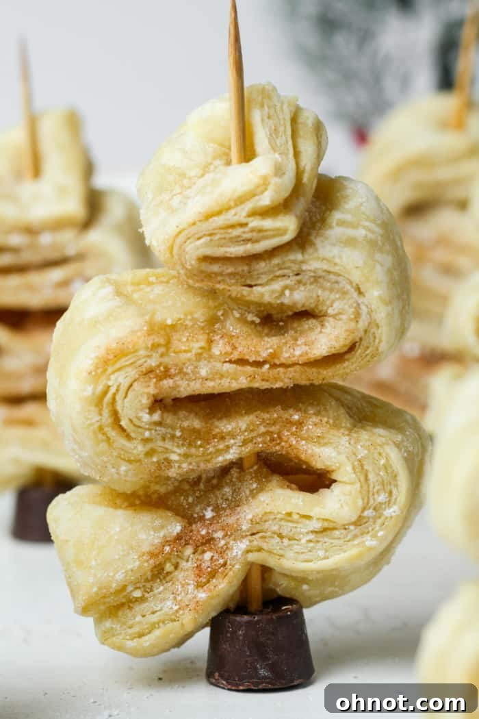 A freshly baked puff pastry Christmas tree on a wooden skewer, standing upright with a Rolo candy base.